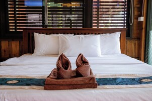 A neatly made bed with a brown towel folded on top, white pillows, and a patterned bedspread.