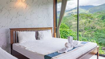 Un dormitorio con una cama grande, una mesita de noche, una lámpara de pared y vistas a un paisaje montañoso.