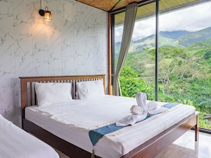 A bedroom with a large bed, a nightstand, a wall-mounted lamp, and a view of a mountainous landscape. - Saiwaree Farmstay (Bo Kluea)