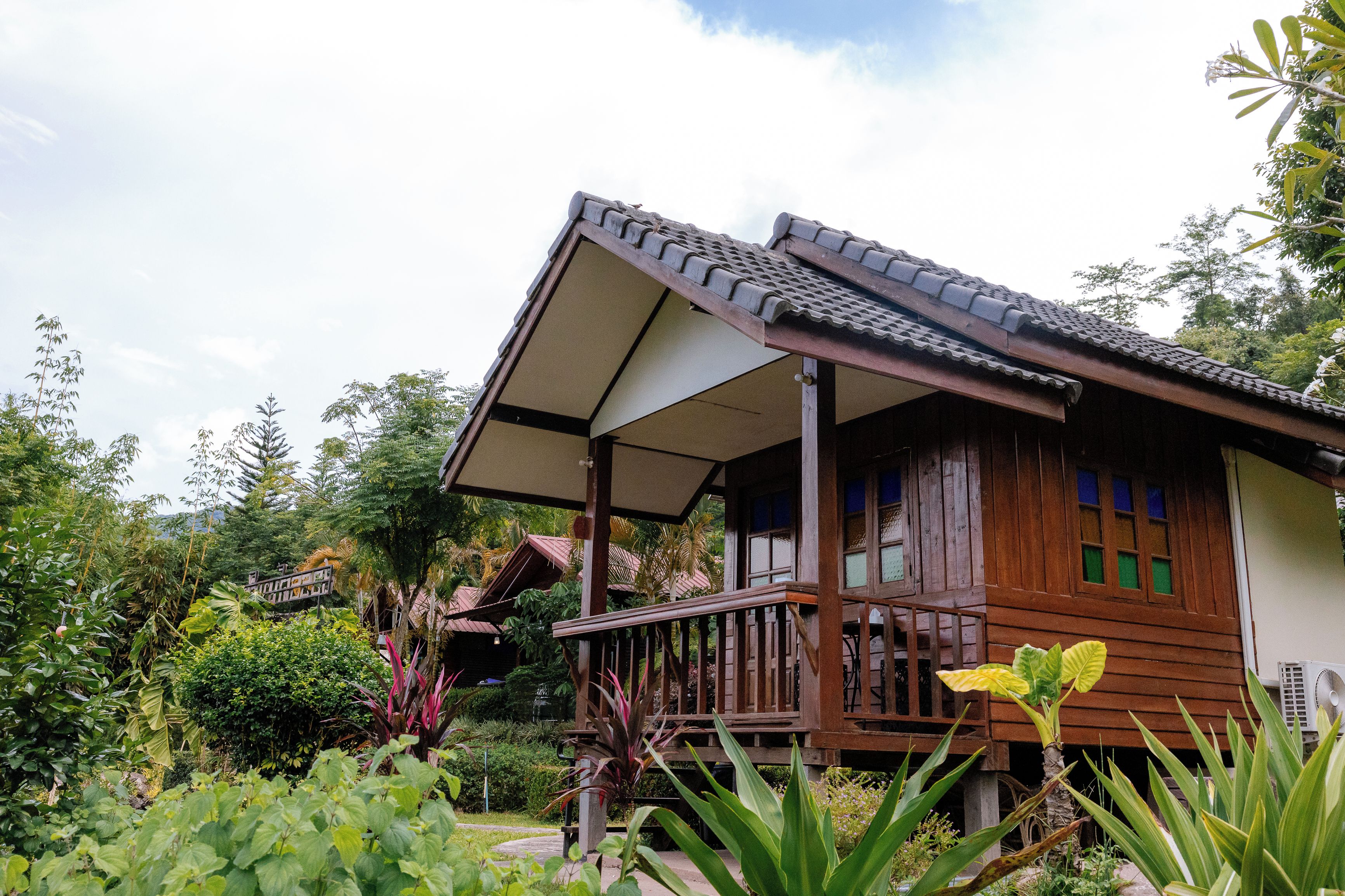 A wooden house with a porch, surrounded by lush greenery.
