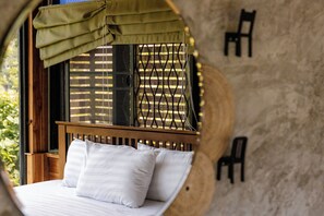 A bed with white bedding and a wooden headboard, a window with a metal grid, and a circular wall design. - Saiwaree Farmstay (Bo Kluea)