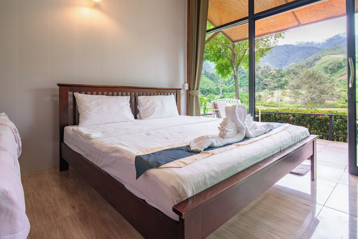 A bedroom with a large bed, a view of the outdoors, and a ceiling light.