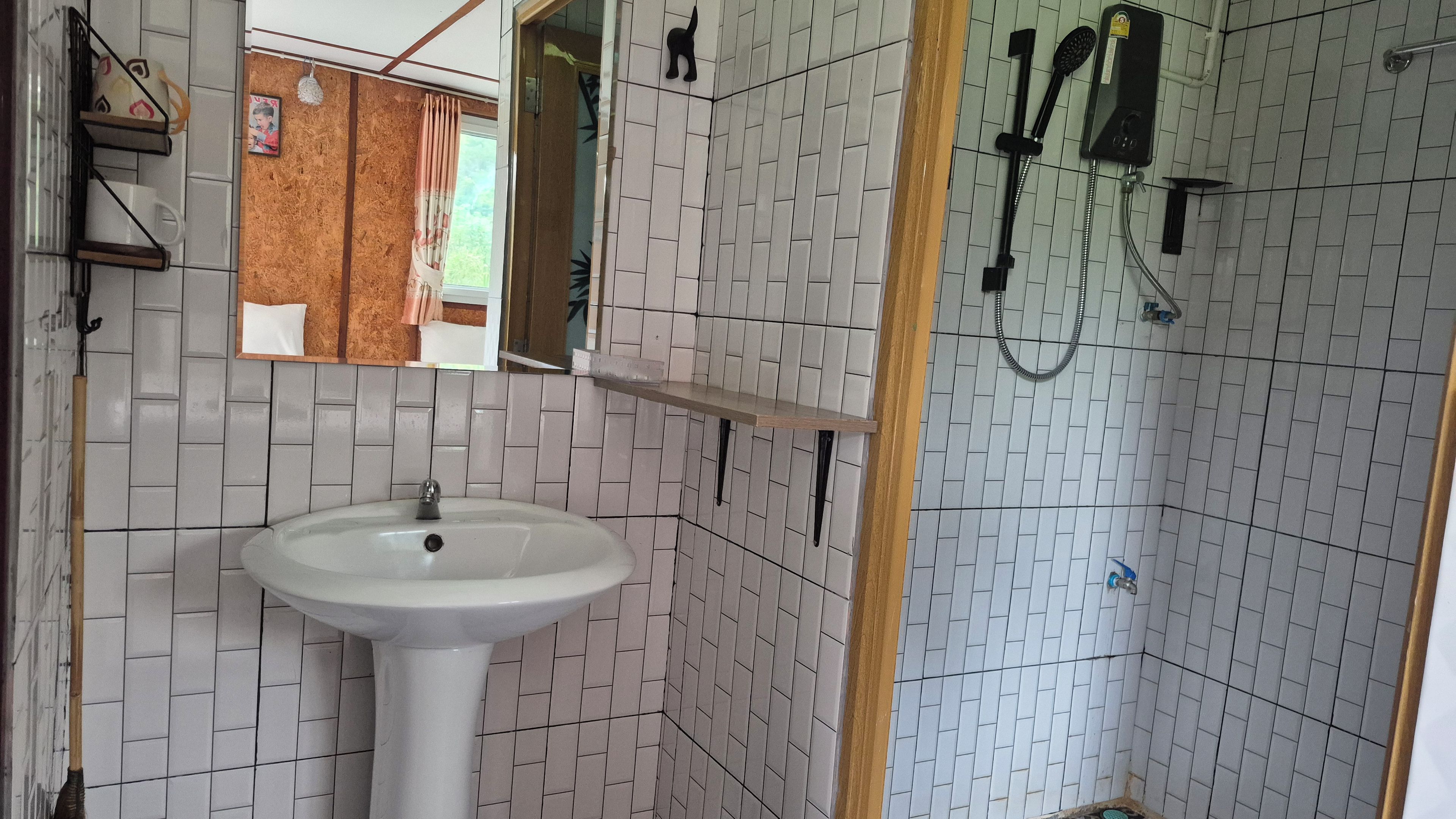 Et badeværelse med en hvid vask, et spejl og en bruseniche.