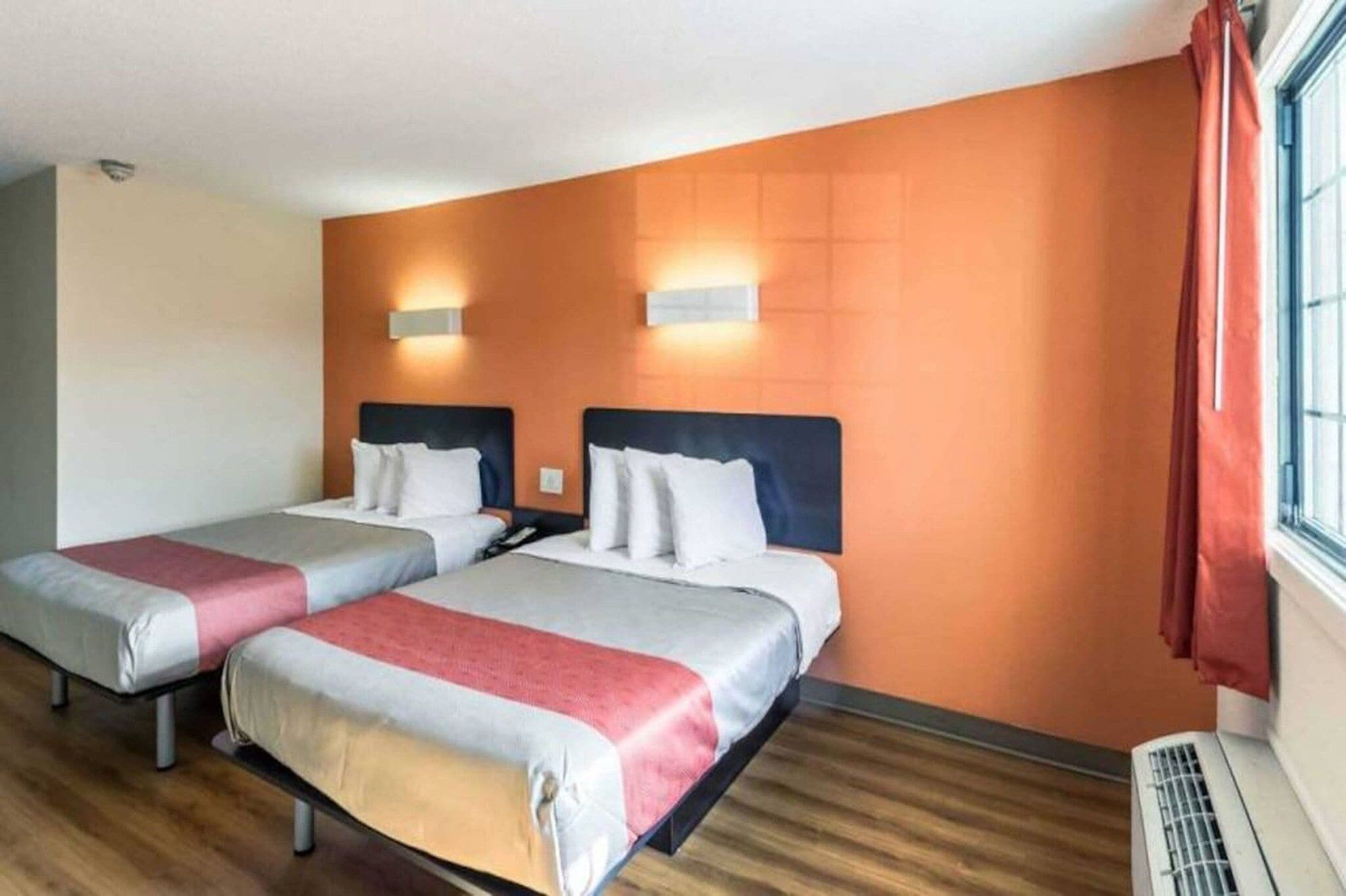 Een hotelkamer met twee bedden, een raam met gordijnen en een wandradiator.