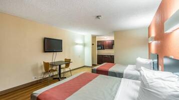 A hotel room with two beds, a television, a small table with chairs, and a kitchenette in the background.