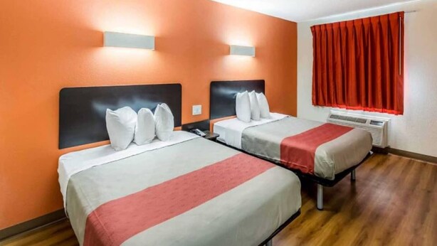 A hotel room with two beds, each with a headboard, white bedding, and a red accent.