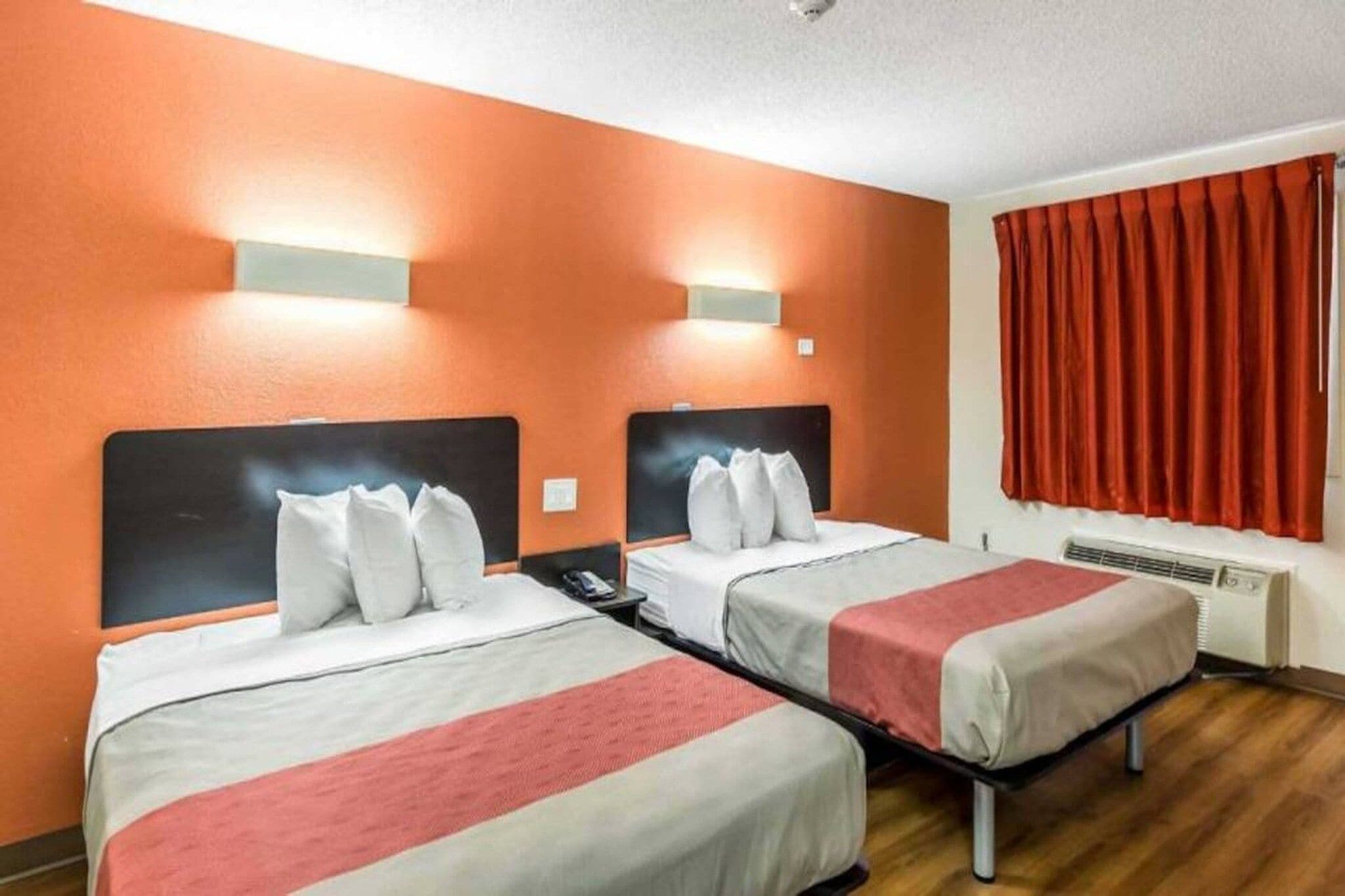 A hotel room with two beds, a red curtain, and a wall-mounted heater.