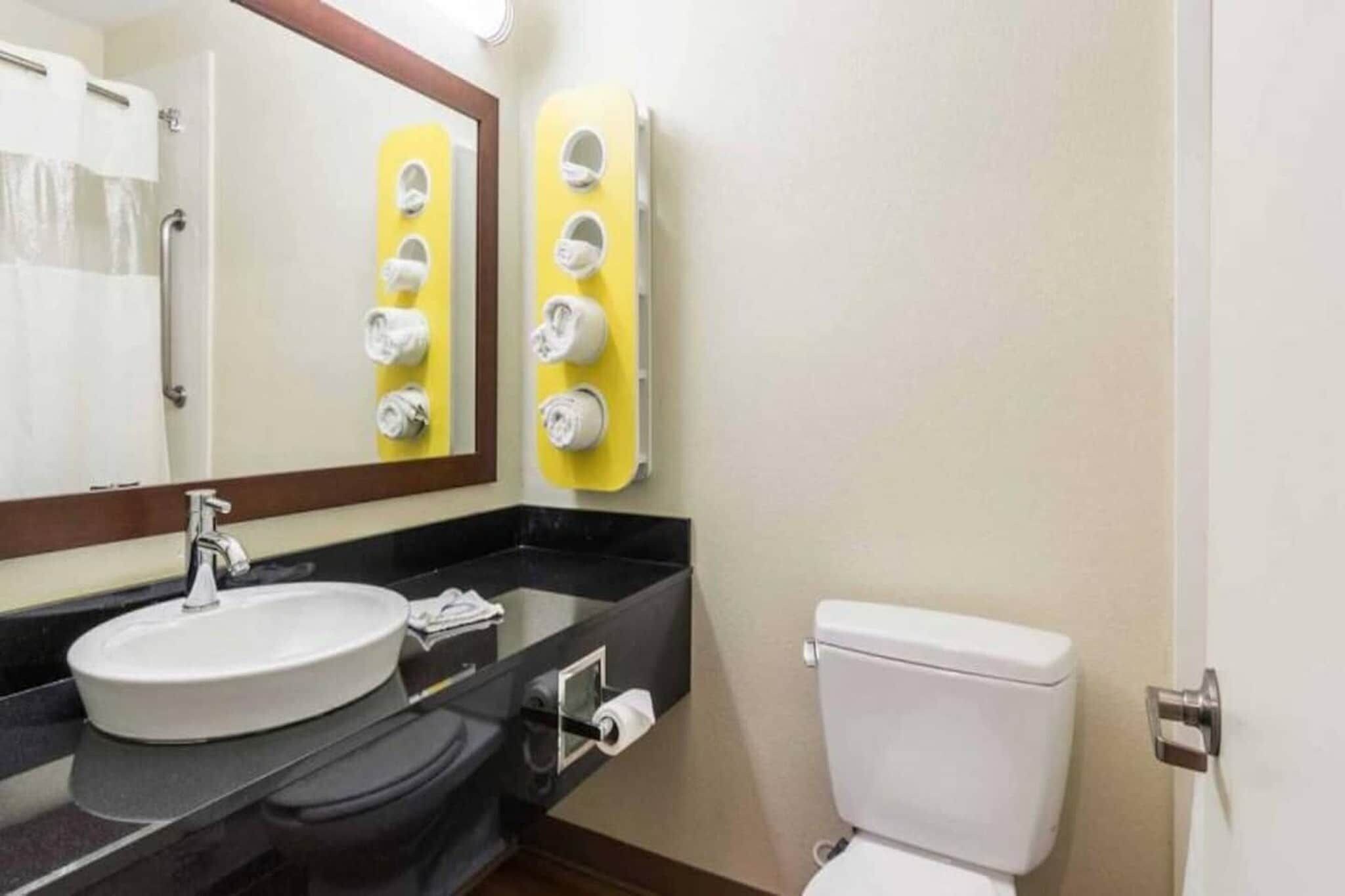 Un baño con lavamanos, espejo, dispensador de toallas y retrete.