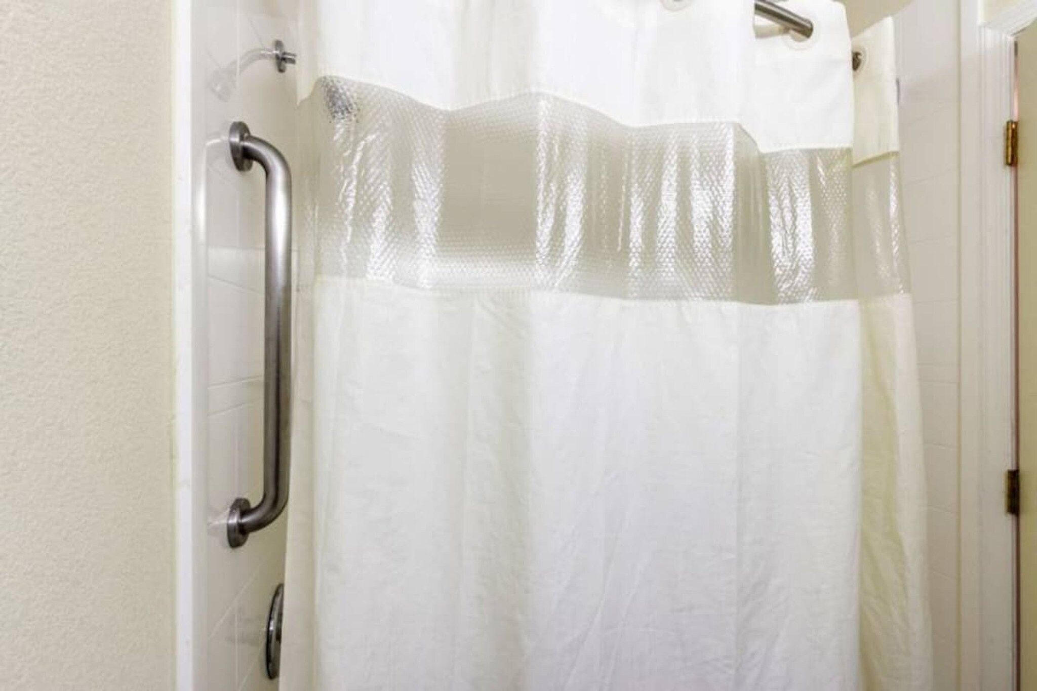A bathroom with a white shower curtain, a grab bar, and a white door.