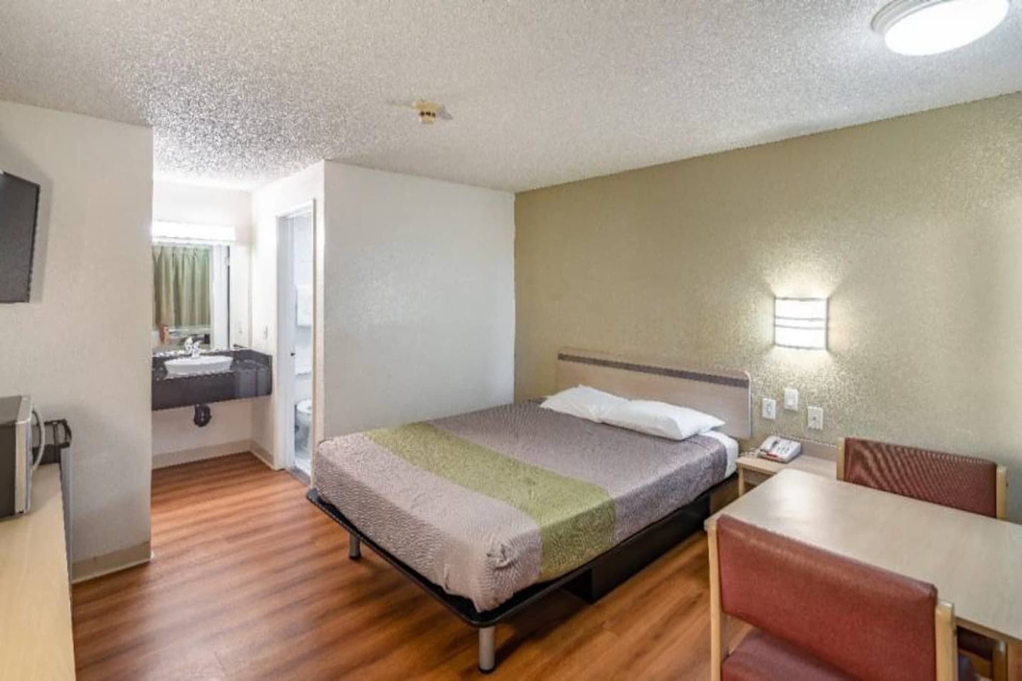 A hotel room with a bed, a desk, and a chair. There is a bathroom visible through an open door.