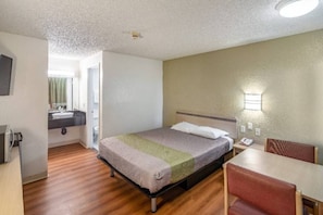 Habitación de hotel con una cama, un escritorio y una silla. Se ve un baño a través de una puerta abierta.