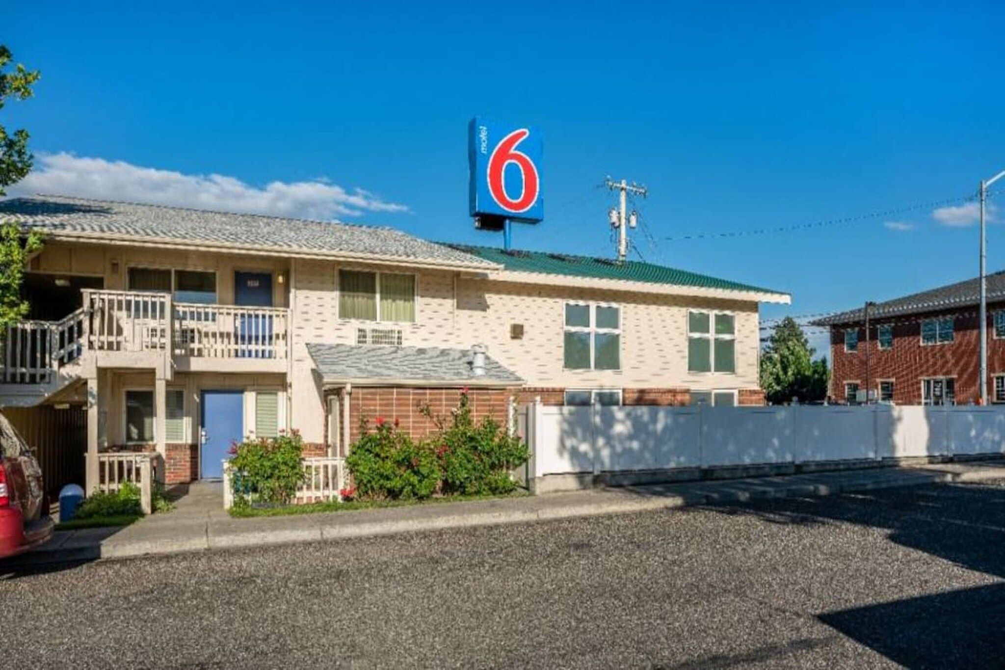 Un motel con un llamativo letrero con el número '6', una estructura de dos pisos con balcón y un camino de grava.