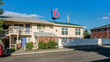 Un motel con un llamativo letrero con el número '6', una estructura de dos pisos con balcón y un camino de grava.