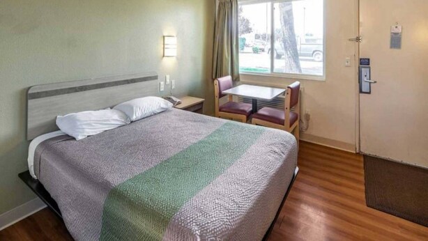 Habitación de hotel con cama, una pequeña mesa con sillas, ventana con cortinas y puerta con cerradura.