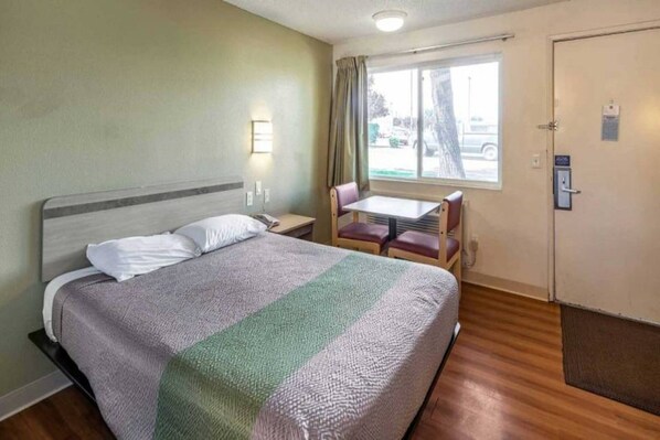 A hotel room with a bed, a small table with chairs, a window with curtains, and a door with a lock. - 1 Queen Bed | Non-Smoking (Clarkston)
