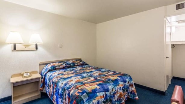 A hotel room with a bed, bedside lamps, a small table, and a door to a closet. - 1 Queen Bed | Mob Acc RI Shwr Nsmk Micfridg (Moses Lake)