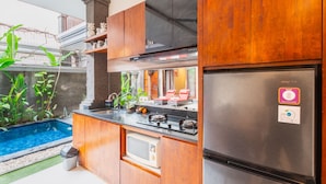 A compact kitchen with a built-in microwave, a stainless steel refrigerator, and a small sink. - Cozzy Dewa Villa Sunset Road (Badung)