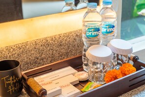 Una bandeja con artículos de aseo que incluye un portalápices para cepillos de dientes, una caja de cepillos, una botella de agua, una botella de champú, un gorro de ducha y una bolsita de jabón.