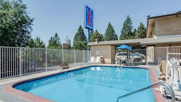Una piscina con área cercada, sillas de descanso y un edificio con un cartel que dice '6 Welcome'.
