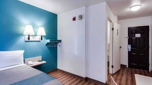 Una habitación de hotel con cama, escritorio, lámpara, perchero y puerta.