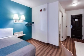 Una habitación de hotel con cama, escritorio, lámpara, perchero y puerta.