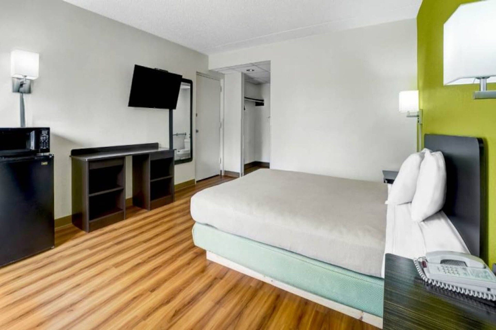 Una camera d'albergo con un letto, una scrivania con un computer, una TV a parete e un telefono sul comodino.