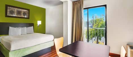 Una camera d'albergo con un letto, un tavolo, una sedia, una finestra con tende e un condizionatore d'aria a parete.