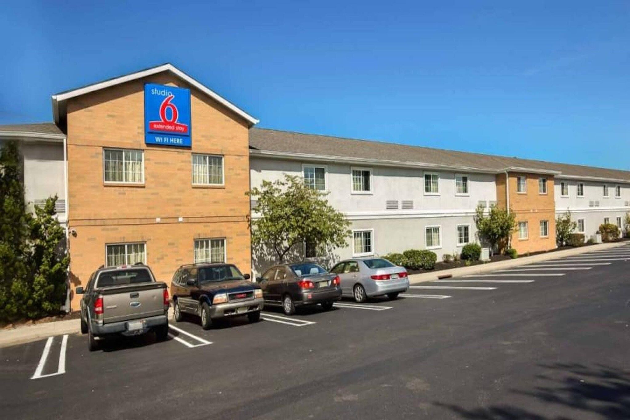 A hotel with a sign indicating Wi-Fi availability, a parking lot with several cars, and a clear blue sky.