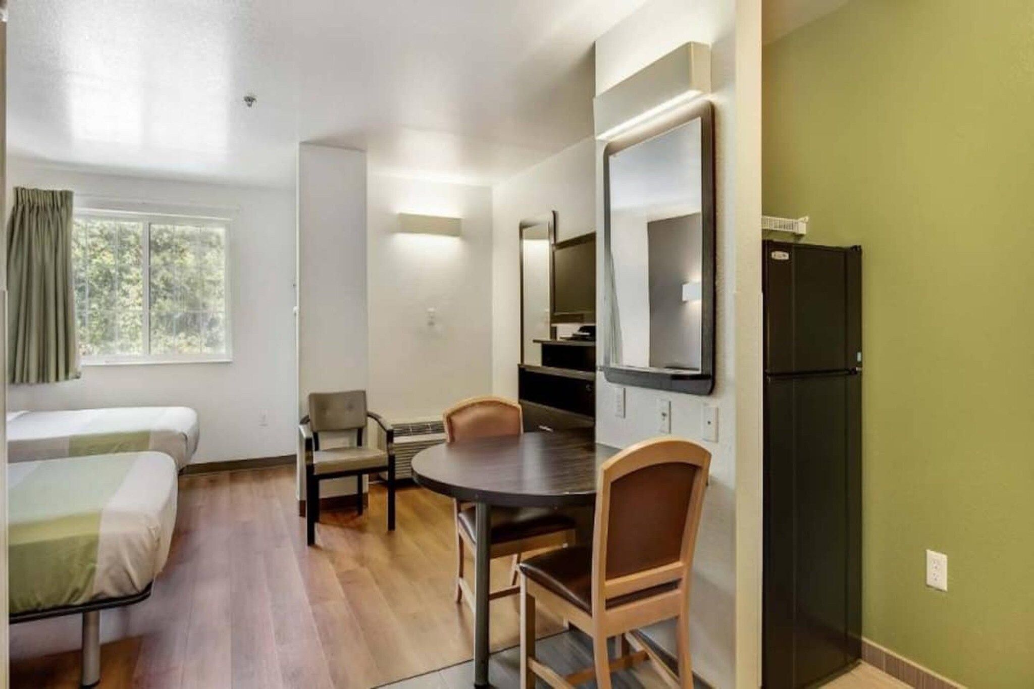 Una habitación pequeña con cama, una mesa, dos sillas, televisor y refrigerador.