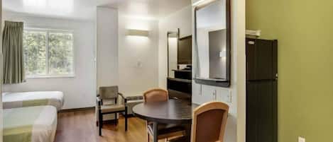 A compact room with a bed, a table, two chairs, a television, and a refrigerator.