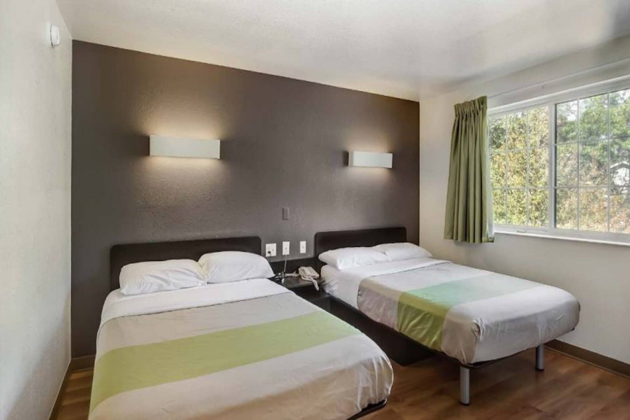 Ein Hotelzimmer mit zwei Einzelbetten, einem Nachttisch mit Telefon und einem Fenster mit Vorhängen.