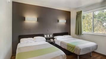 Ein Hotelzimmer mit zwei Einzelbetten, einem Nachttisch mit Telefon und einem Fenster mit Vorhängen.
