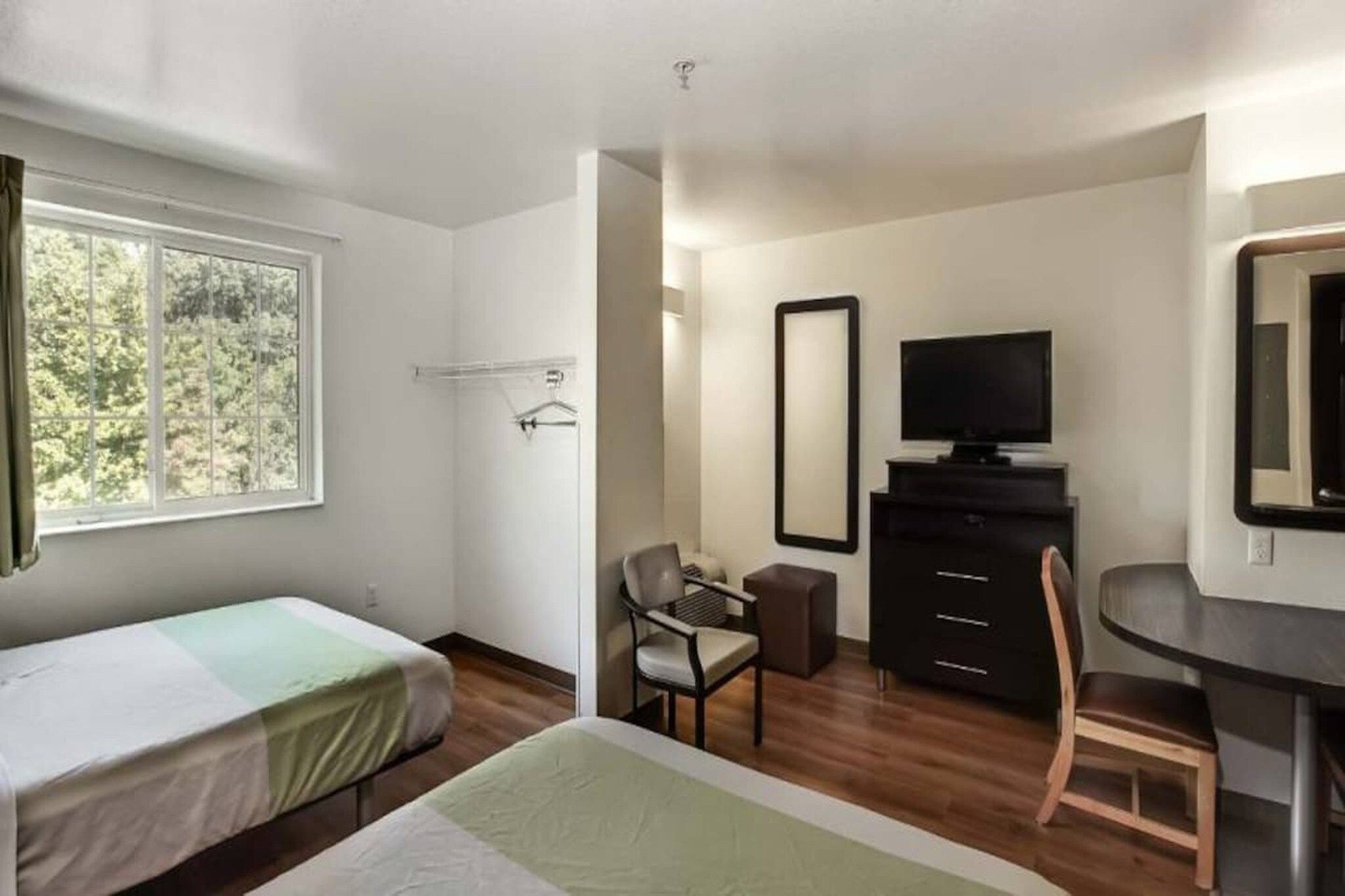 Ein Hotelzimmer mit Bett, Schreibtisch, Stuhl, Fernseher und Spiegel.