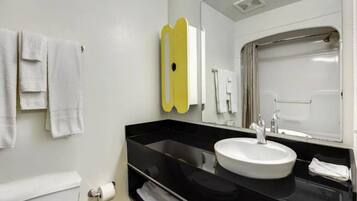 A modern bathroom with a black countertop, white sink, and a mirror with a yellow accent.