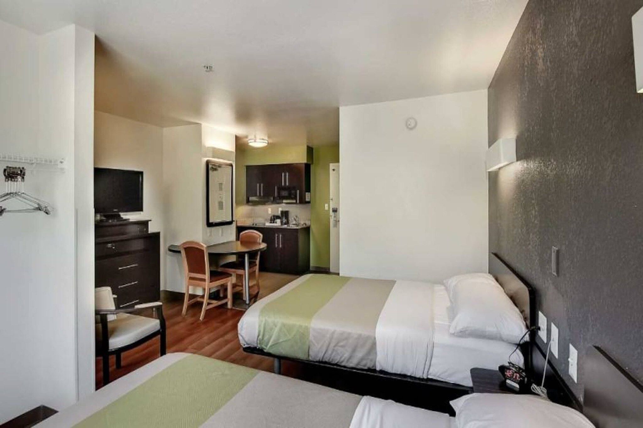 Una habitación de hotel con dos camas, un escritorio, una silla y una kitchenette.