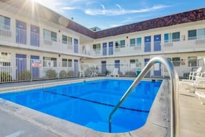 A hotel with a swimming pool, multiple balconies, and a fenced area.