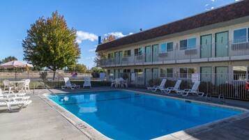Ein Motel mit Schwimmbad, Liegestühlen und einem eingezäunten Patio.
