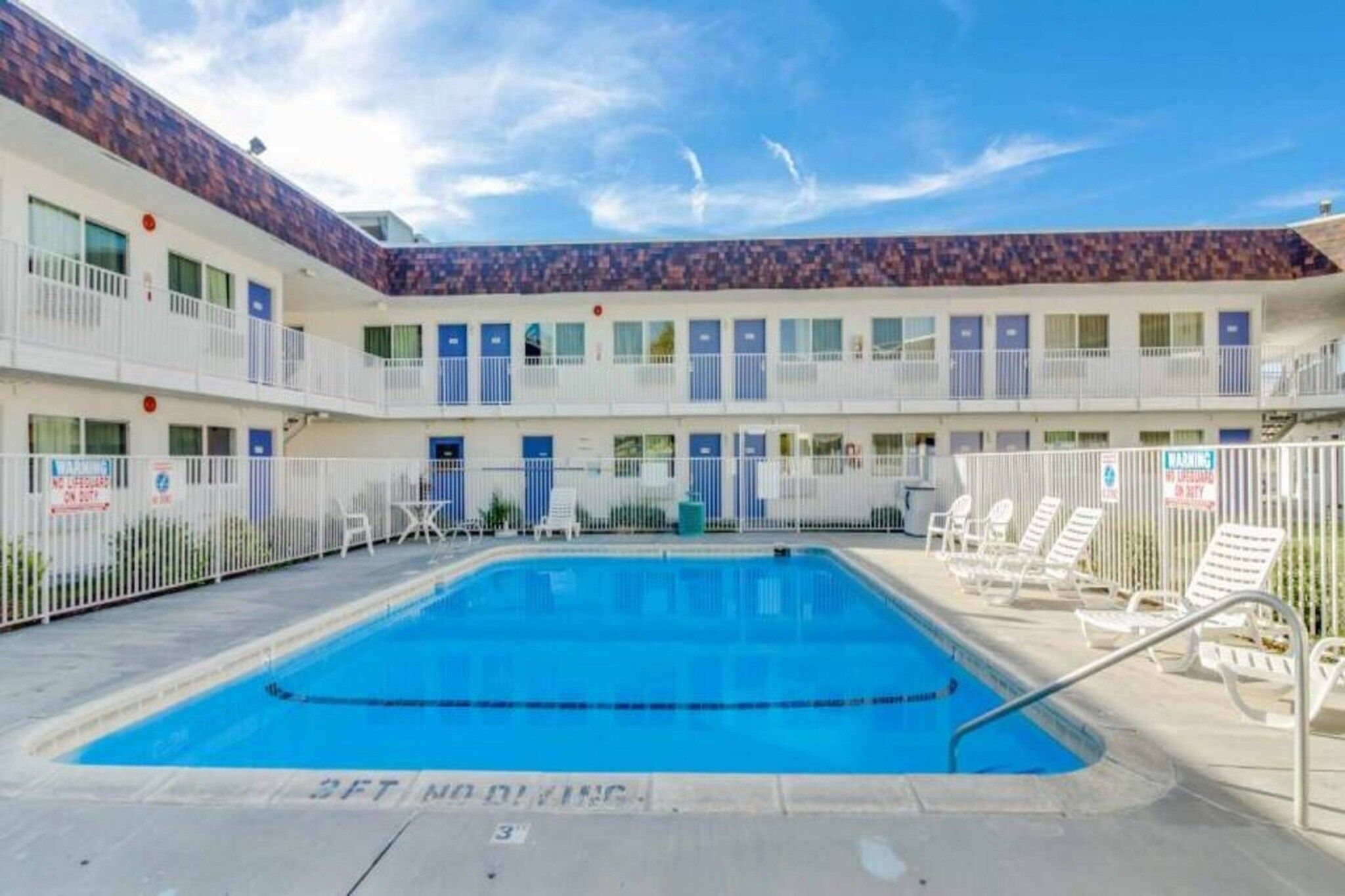 A hotel with a swimming pool, multiple balconies, and a fenced area with lounge chairs.