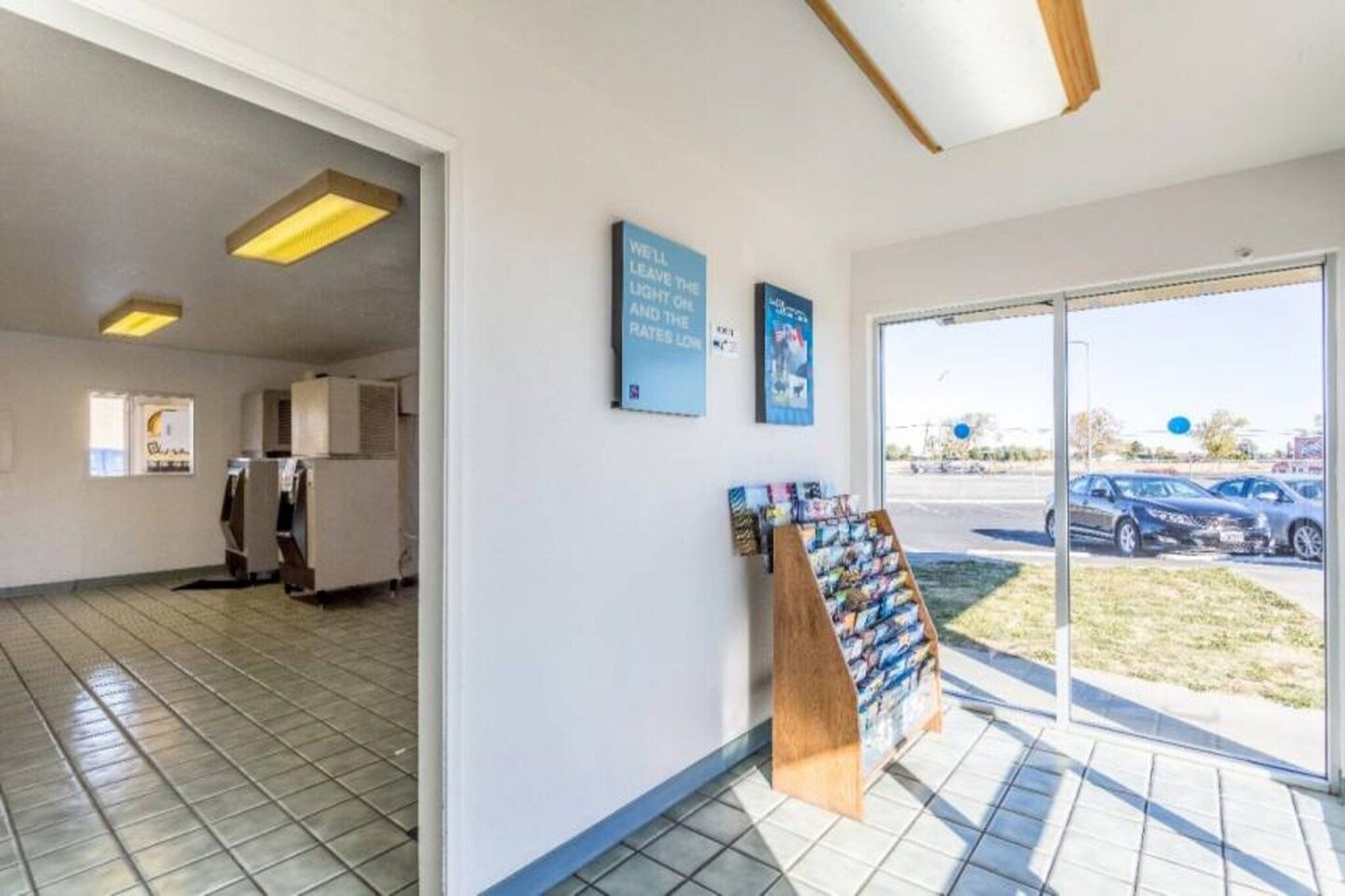 Interior comercial com piso de azulejos, máquina de vendas automática e uma grande janela com vista para carros estacionados.