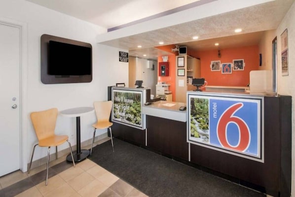 Un'area reception di un hotel con un bancone, una TV a muro e una segnaletica che indica la stanza numero 6.