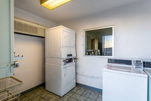 A compact laundry room with a stacked washer and dryer, a small window, and a metal laundry basket.