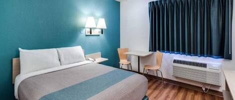 A hotel room with a bed, desk, chairs, and an air conditioning unit.