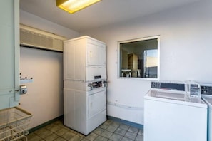 A compact laundry room with a stacked washer and dryer, a small window, and a metal laundry basket.