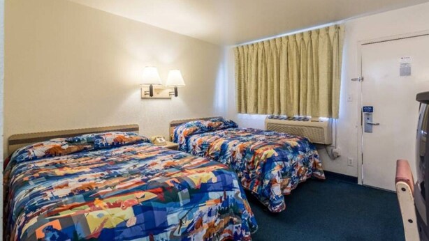 Een hotelkamer met twee bedden, een raam met gordijnen, een wandlamp en een deur met een bordje.