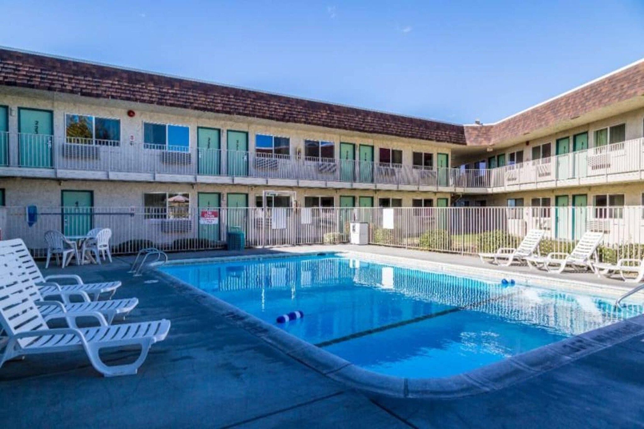 A motel with a swimming pool, multiple balconies, and lounge chairs.
