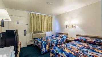 A hotel room with two beds, a desk, a chair, a television, an air conditioning unit, and a window with curtains.