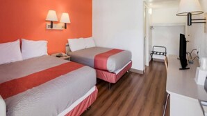 Een hotelkamer met twee bedden, een bureau, een televisie en een badkamer zichtbaar door een open deur.