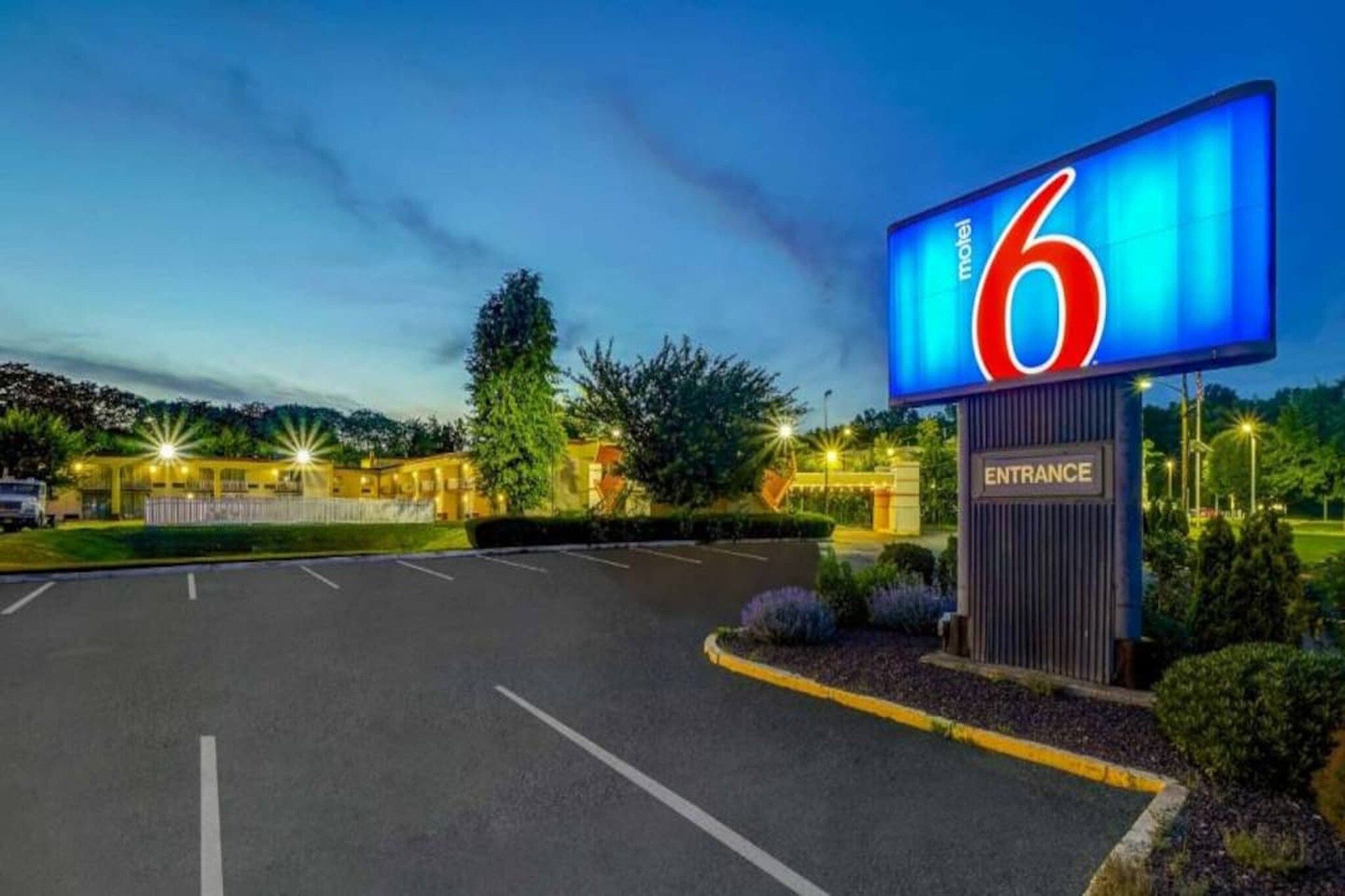 L'ingresso di un motel, con un grande cartello, un parcheggio e un edificio sullo sfondo.