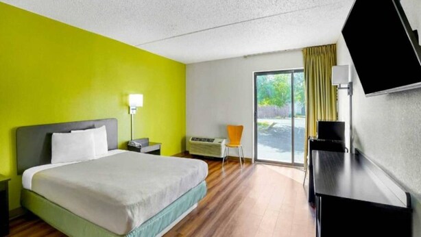 Ett hotellrum med en säng, ett skrivbord, en stol, en tv och ett fönster med gardiner.