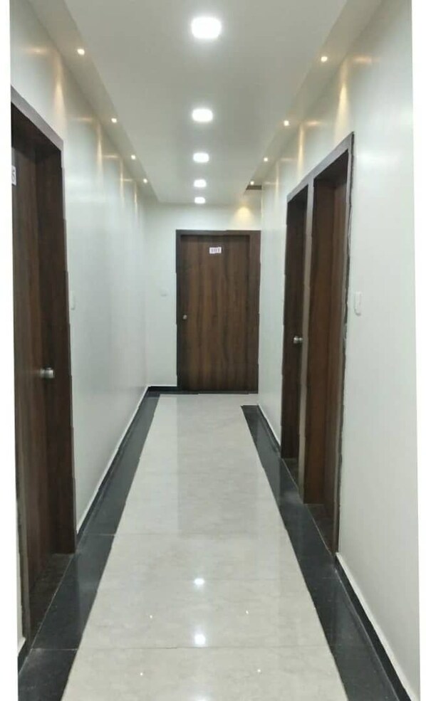 A corridor with a tiled floor, wooden doors, and recessed lighting.